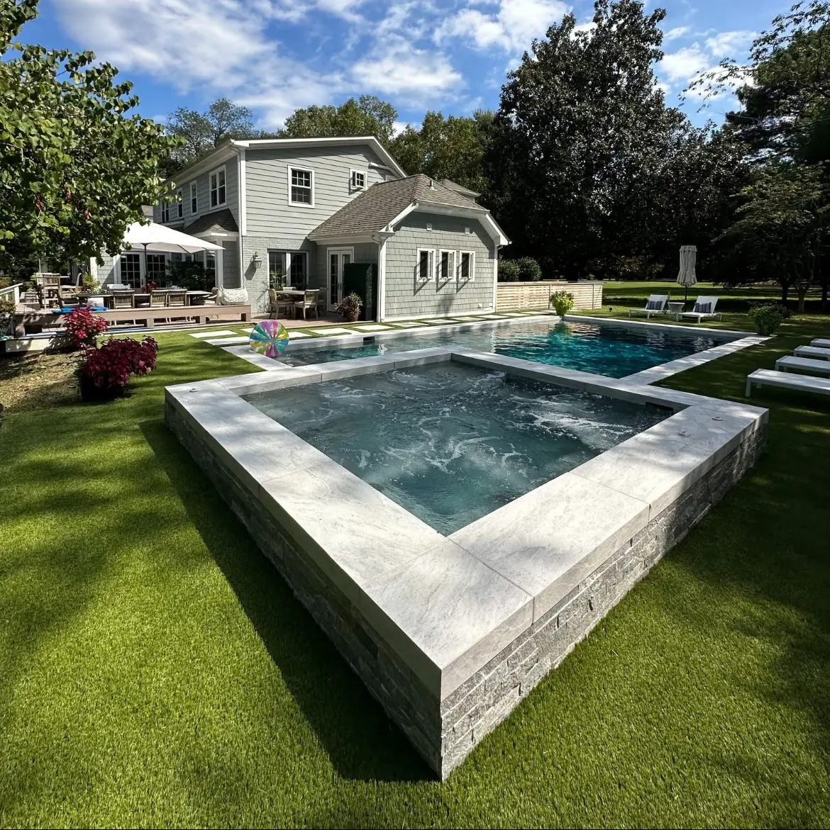 Modern raised spa with stone facade beside a backyard pool