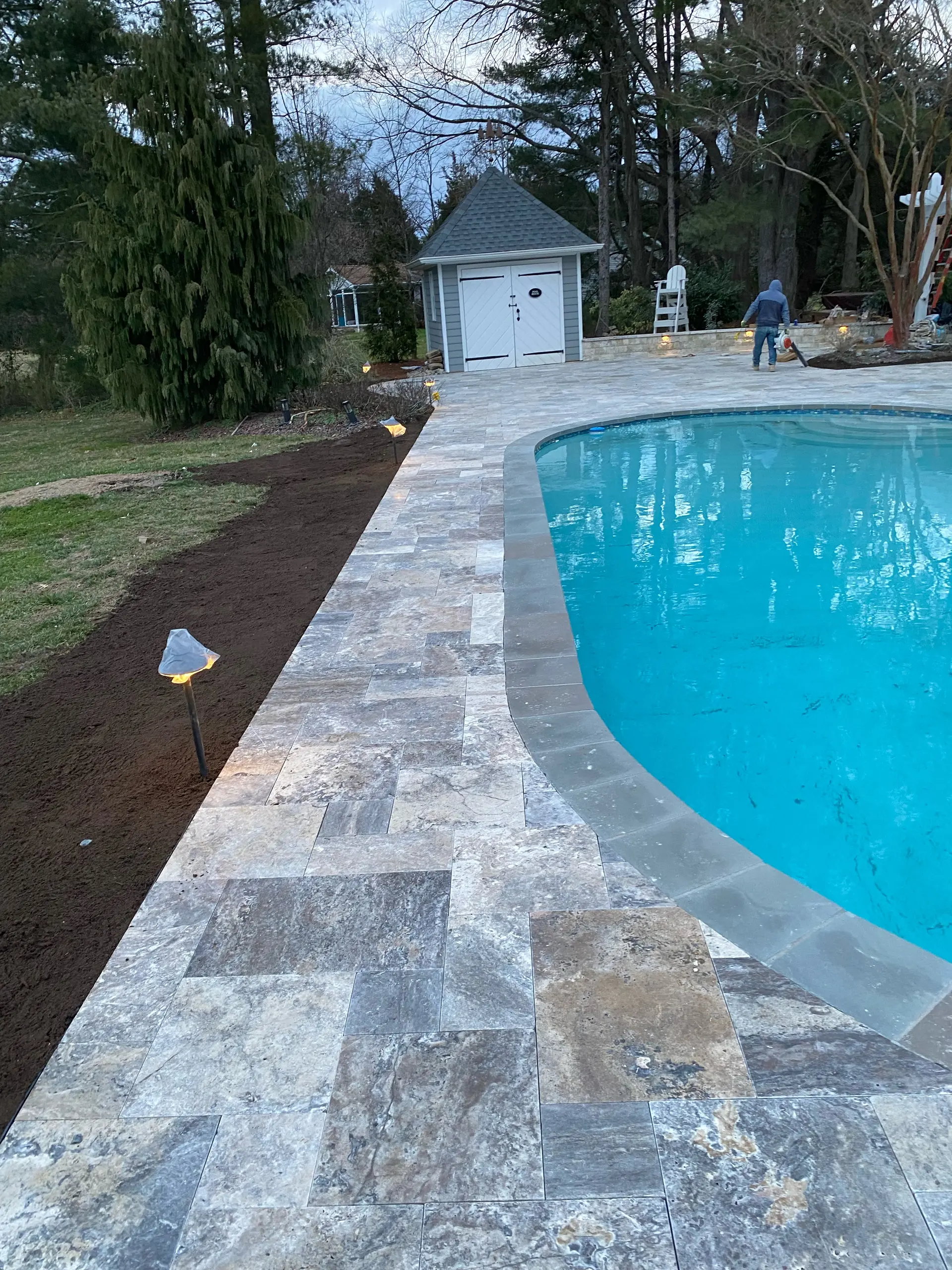 Travertine pool deck at dusk with warm landscape lighting